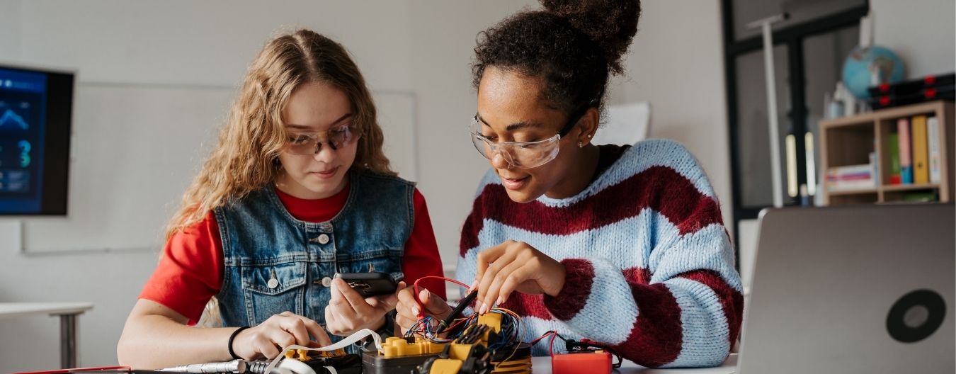 26 – LCWAG Loudoun Commission on Women & Girls Hosts a Successful STEM Expo Two students wearing safety goggles collaborate on a STEM project, working with electronics and wiring at a classroom table.