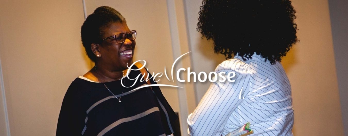 27 – LCWAG Loudoun Commission on Women & Girls Records a Successful Give Choose Day Two women smiling and talking at a community event, with “Give Choose” text and the Loudoun Coalition Women and Girls logo displayed.
