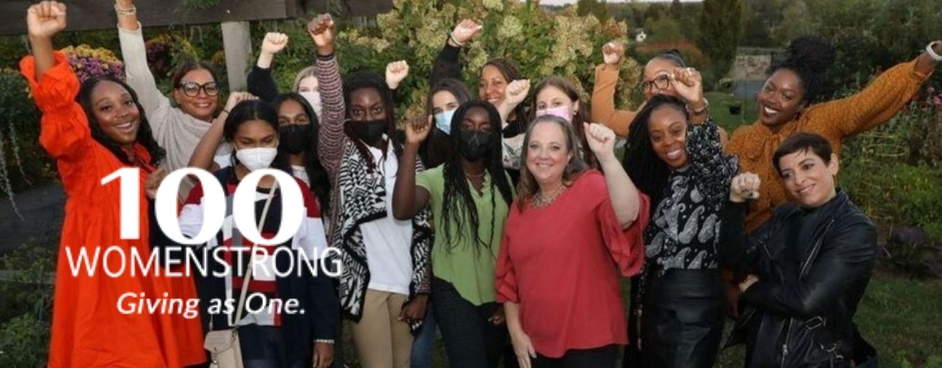 A group of women receiving the 2022 100WomenStrong Grant with a text on the side “100WomenStrong Giving as One”